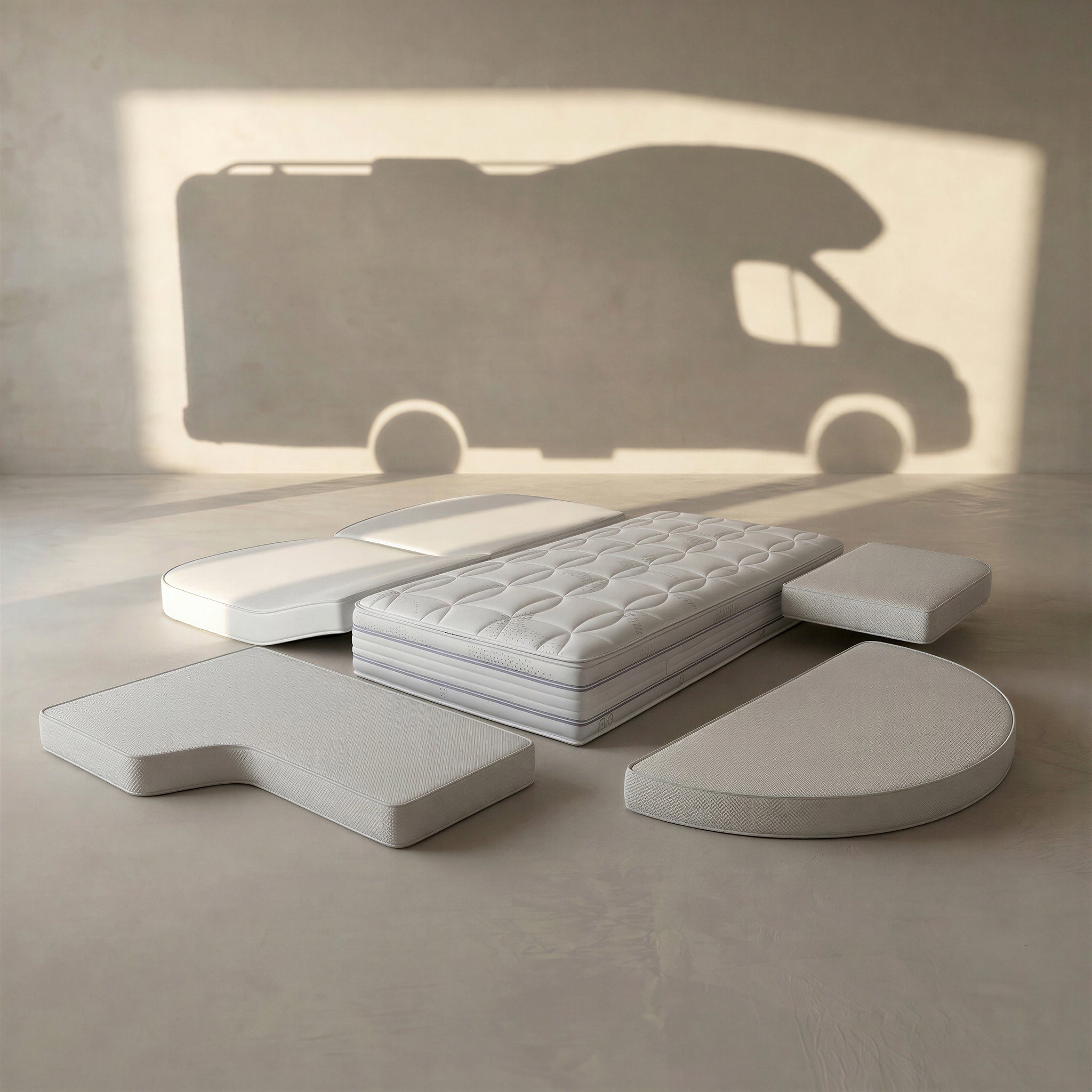 enjoy Camper-Matratze nach Maß: individuell geformte Matratzenteile mit Schrägen und Rundungen, im Hintergrund die Silhouette eines Wohnmobils