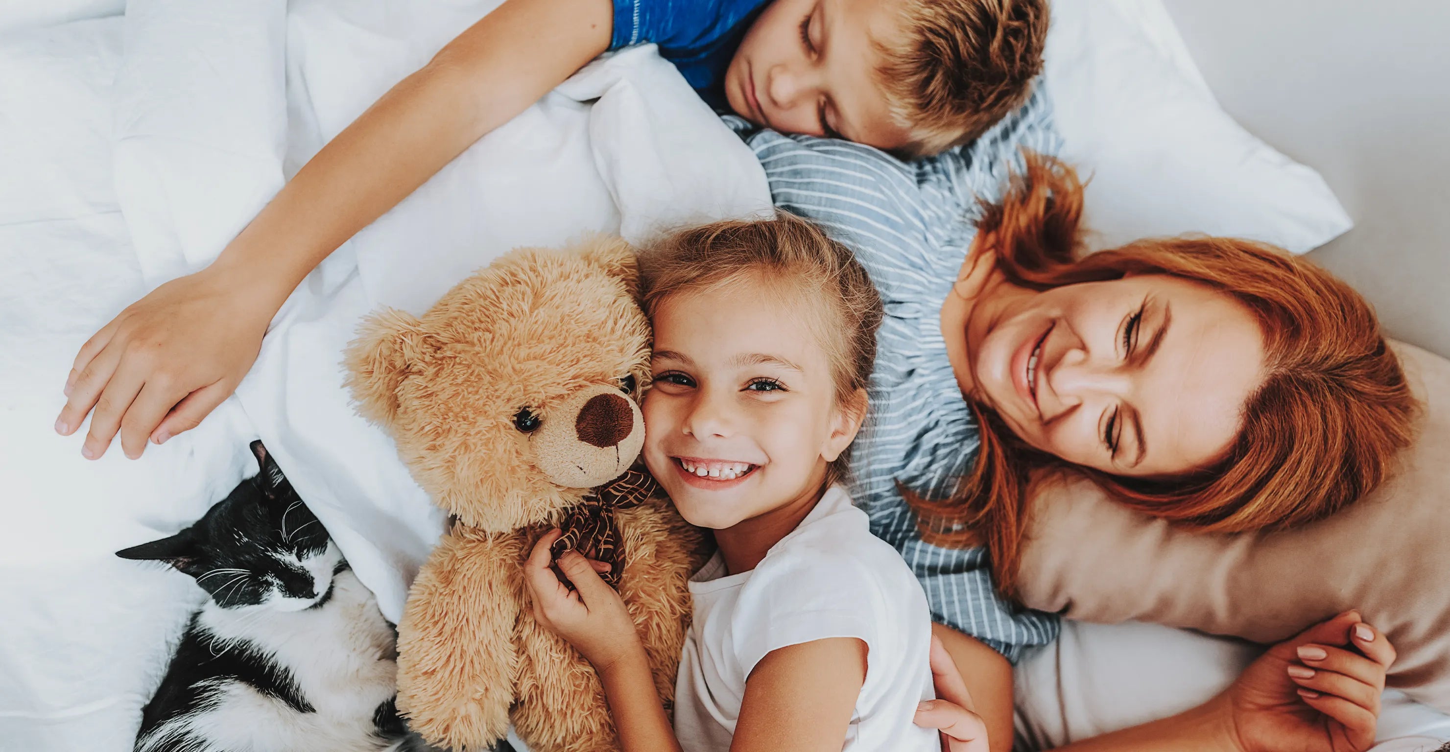 Eltern und Kinder liegen gemeinsam auf einem großzügigen familienbett von enjoy schlafsysteme im modernen schlafzimmer