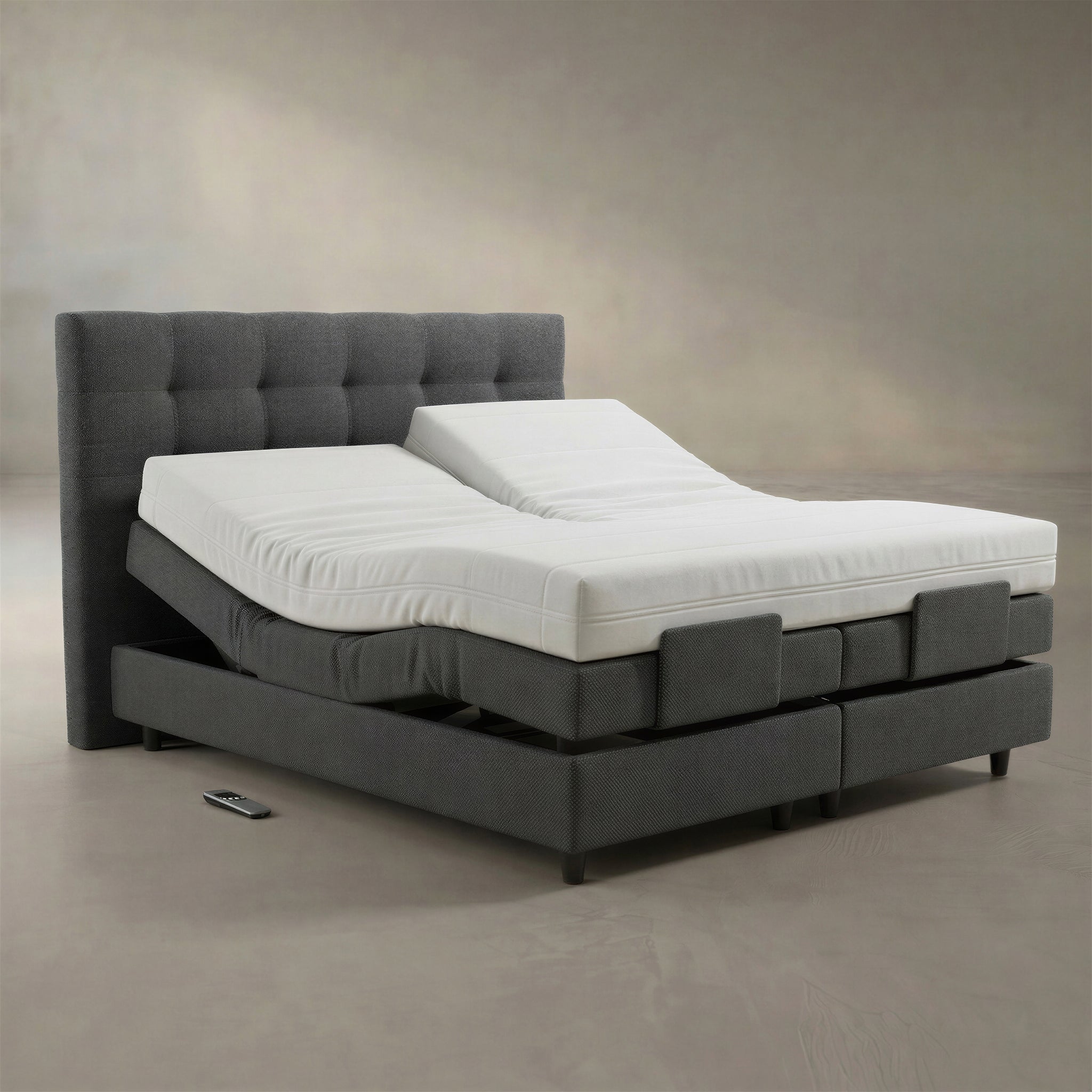 Motorisiertes enjoy Boxspringbett in Anthrazit vor neutralem Studiohintergrund, Kopfteil elektrisch hochgefahren, Split-Rahmen sichtbar, Funk-Fernbedienung liegt davor auf dem Boden