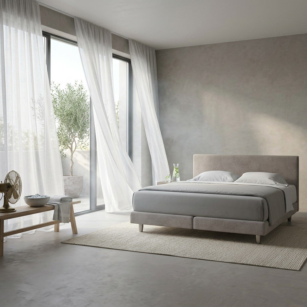 enjoy.neo Boxspringbett in hellem, luftigem Schlafzimmer mit wehenden Vorhängen, Ventilator und Eiswasser als Sinnbild für kühle Sommernächte